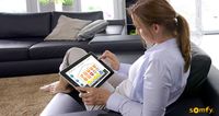 Eine Frau sitzt mit einem Tablet auf einer Couch und steuert darüber die Smart Home gesteuerten Produkte.
